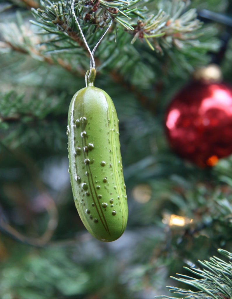 A shiny green glass pickle ornament hanging on a Christmas tree branch, representing the quirky German Christmas Pickle Tradition