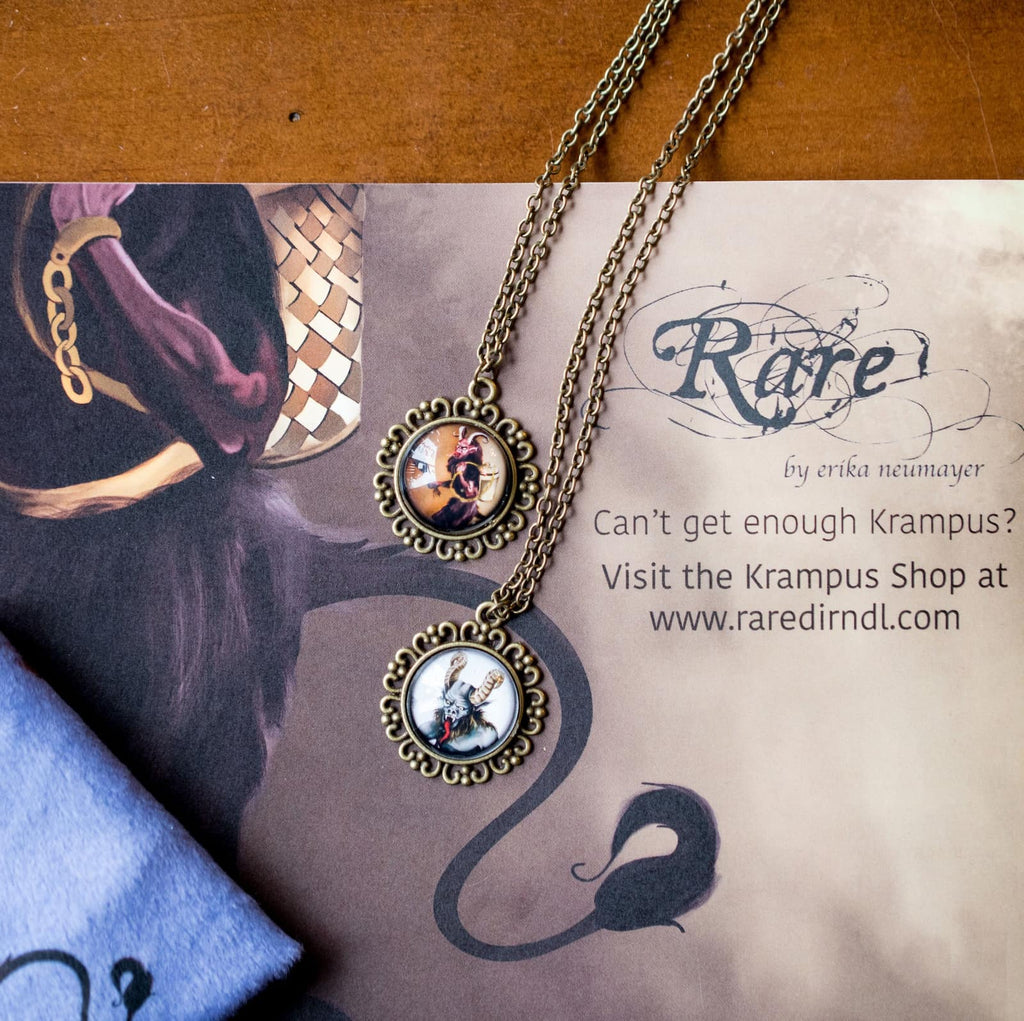 Two vintage-style Krampus pendant necklaces with bronze chains displayed on a Rare Dirndl promotional card.